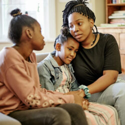 Three Black girls hold each other on a sofa.