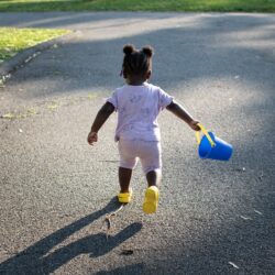 A child carrying a bucket Description automatically generated